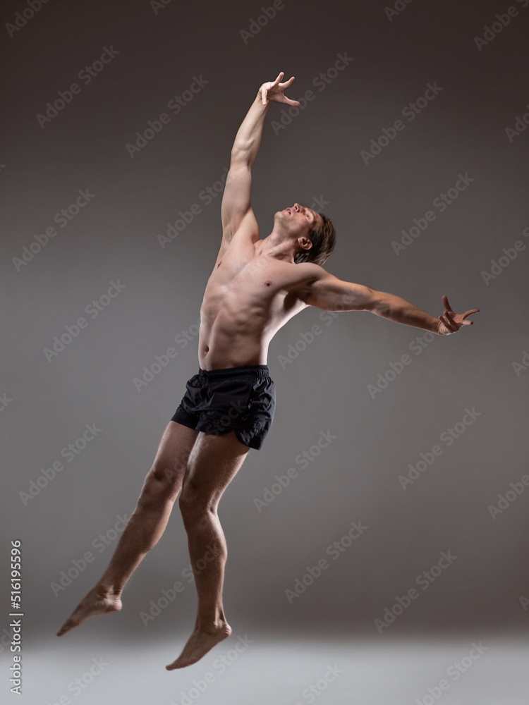 Fototapeta premium Muscular man in an artistic pose, portrait on a gray background. The guy is an athlete in a jump or fall. Expressive pose