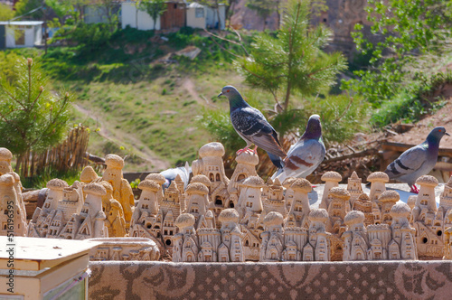 Pigeons standing on Cappadocia souvenirs, gifts at outdoor gift shop. Background Turkish village, summer time. Nevsehir, Turkey.
