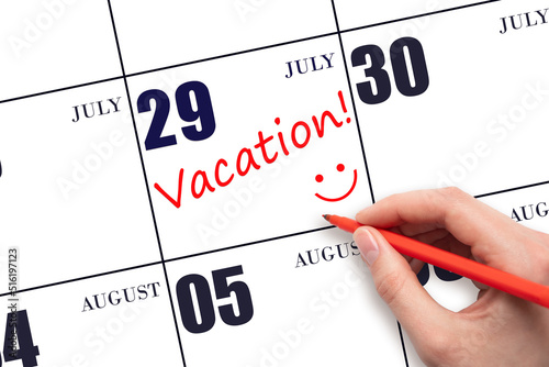 A hand writing a VACATION text and drawing a smiling face on a calendar date 29July. Vacation planning concept. photo