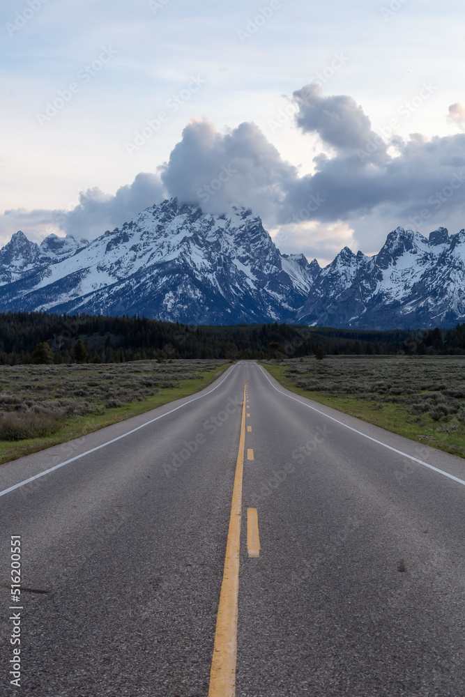 Scenic Road surrounded by Mountains and Trees in American Landscape. Spring Season. Grand Teton National Park. Wyoming, United States. Nature Background. Scenic Road surrounded by Mountains and Trees in American Landscape. Spring Season. Grand Teton National Park. Wyoming, United States. Nature Background.