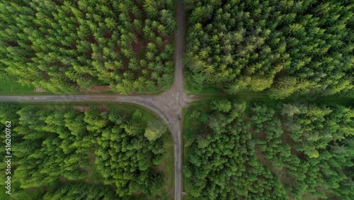 Aerial bird's eye view over a crossroad of two roads in the middle of a dense green forest at daytime. Summer. Aerial top view.