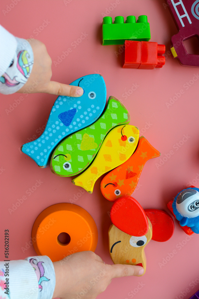 Obraz premium Child is playing with colorful wooden and plastic toys, on pink background
