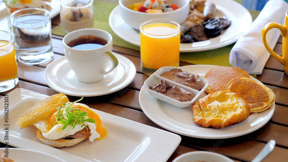 Delicious breakfast in hotel. Table with various food, eggs Benedict, fresh pastry, juices, tea and coffee drinks. Morning food in tropical resort. Dinner in outdoor cafe. 