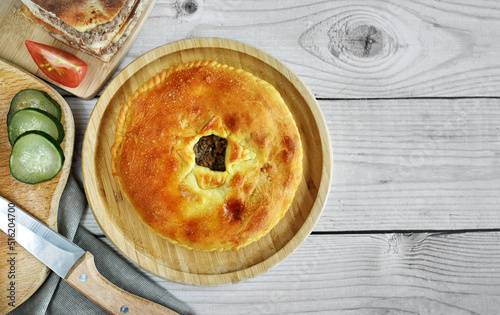 The traditional dish of the peoples of the Caucasus is Karachai khychins (Ossetian pies) with meat on a wooden board. Light wooden background, top view, copy space.