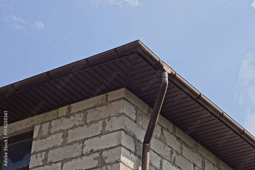 long brown plastic gutter pipe on white brick wall outdoors against blue sky