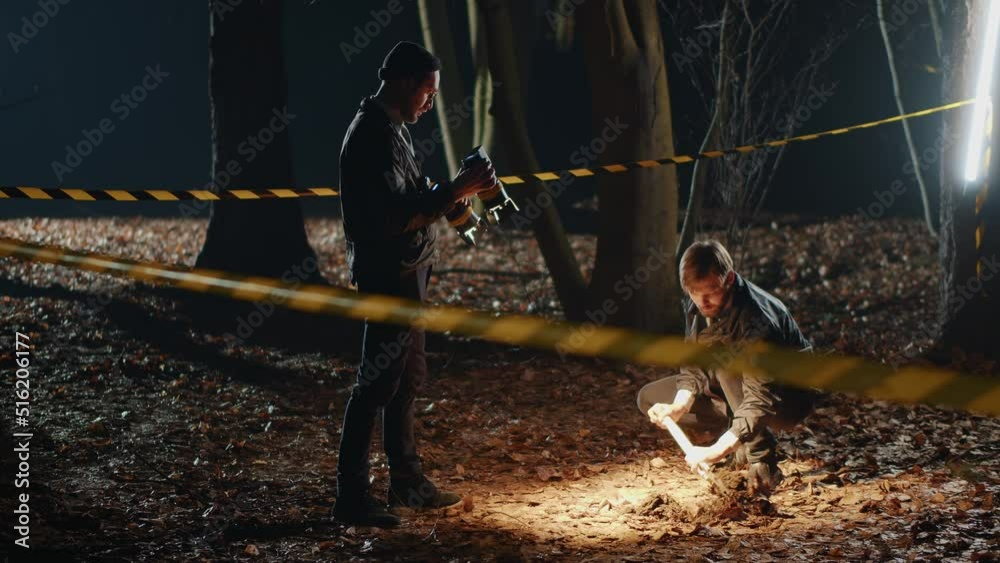 Two Caucasian detectives with shovel in hands digging hole, talking to each others in forest at night. Footage of young smart men at work. Mysterious murder. Strange story. Horror scene