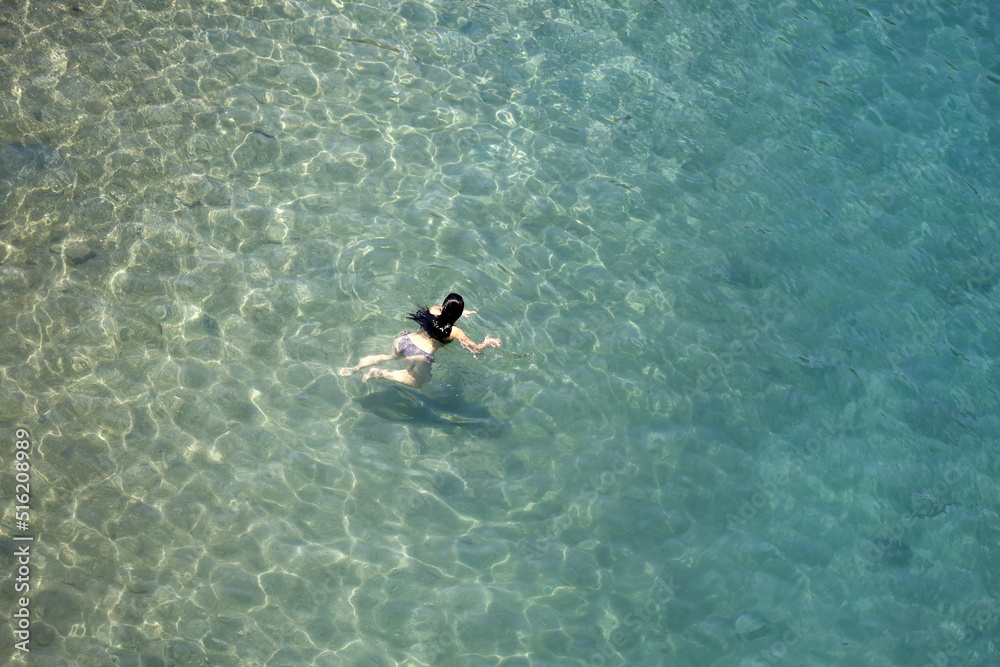 Aerial view to azure sea and woman swimming in transparent water. Girl swimmer, beach vacation in summer