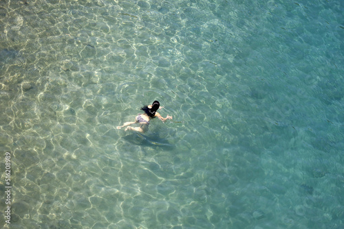 Aerial view to azure sea and woman swimming in transparent water. Girl swimmer, beach vacation in summer