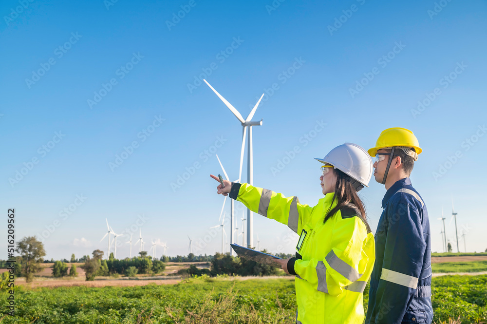 Two engineers working and holding the report at wind turbine farm Power Generator Station on mountain,Thailand people,Technician man and woman discuss about work Two engineers working and holding the report at wind turbine farm Power Generator Station on mountain,Thailand people,Technician man and woman discuss about work