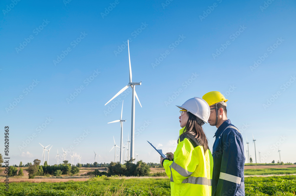 Two engineers working and holding the report at wind turbine farm Power Generator Station on mountain,Thailand people,Technician man and woman discuss about work