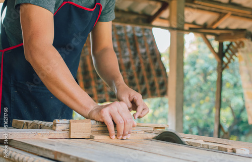 Asian carpenter is using a circular saw to cut wood to construct a storage box on a desk table at his factory. Working as your own boss at home concept