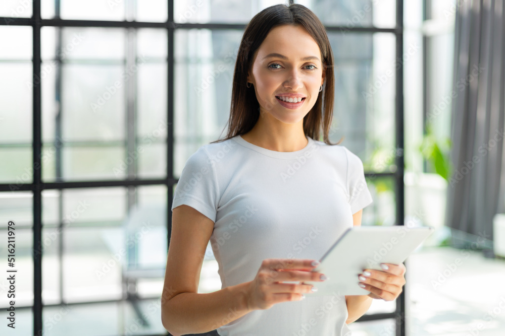 Portrait of young businesswoman holding touch pad while standing in modern office space interior Portrait of young businesswoman holding touch pad while standing in modern office space interior
