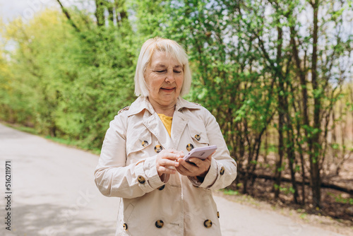 Mature blonde woman in casual clothes browsing smart phone while park of city. Caucasian blogger holding phone pondering thinking on idea for social publication outdoors, Lifestyle concept.