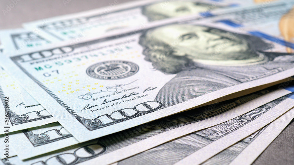 American paper money. Several one hundred dollar banknotes lie on a gray textured surface. Focus on the number 100. Savings economy and the US dollar. Fed and federal funds rate American paper money. Several one hundred dollar banknotes lie on a gray textured surface. Focus on the number 100. Savings economy and the US dollar. Fed and federal funds rate