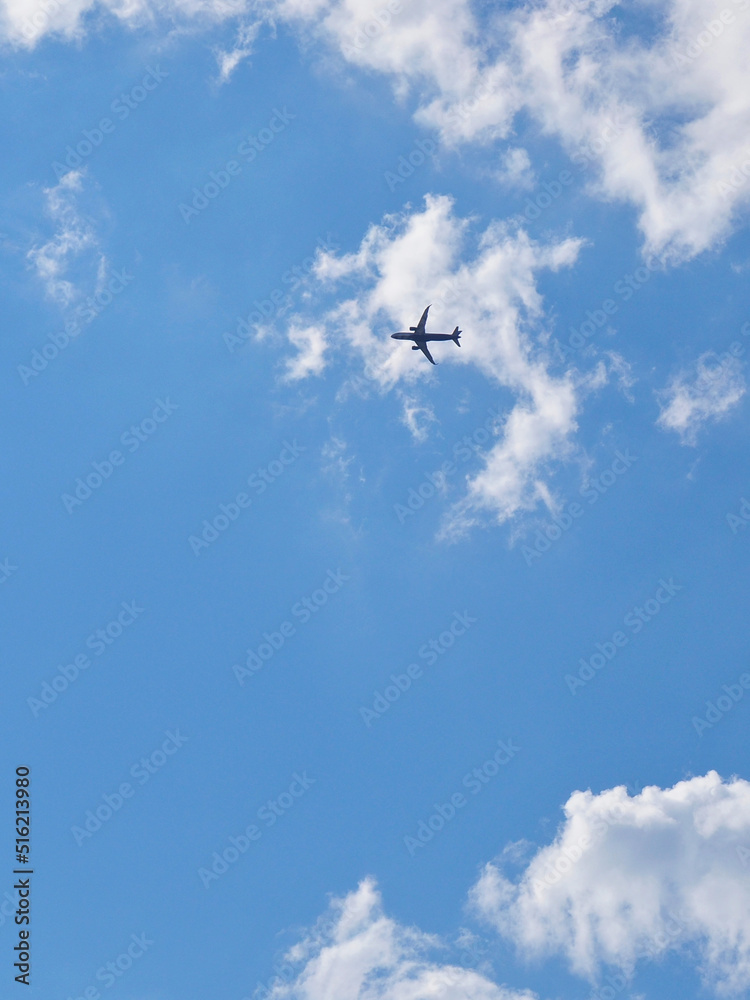 The passenger airplane is flying far away in the blue sky and white clouds. Aircraft in the air. Light vertical background or illustration about international passenger air transportation