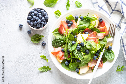 Healthy salad with spinach, jamon, pear and blueberry. Top view on white background.
