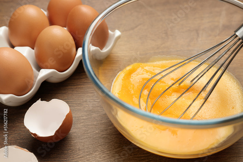 Whisking eggs in glass bowl on wooden table, closeup