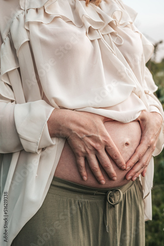 pregnant woman holding her hands on her stomach, close-up
