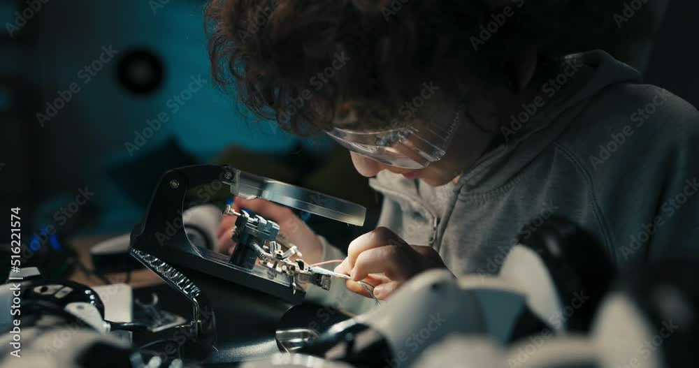 The little engineer sits at desk wearing safety goggles and developing his passion for soldering. The child learns to use equipment to repair electronics, solders cables, wires.