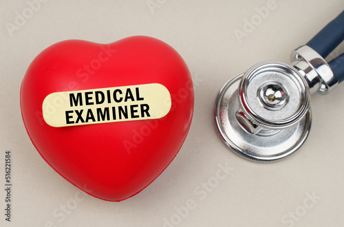 Near the stethoscope lies a heart on which a sticker is pasted with the inscription - MEDICAL EXAMINER photo