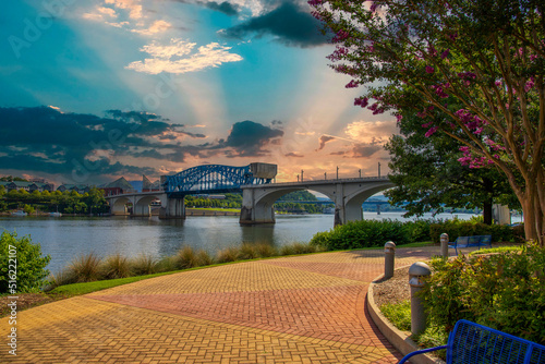 the majestic blue Chief John Ross Bridge over the Tennessee River surrounded by lush green trees and plants with a gorgeous blue sky and powerful clouds at Coolidge park in Chattanooga Tennessee USA photo