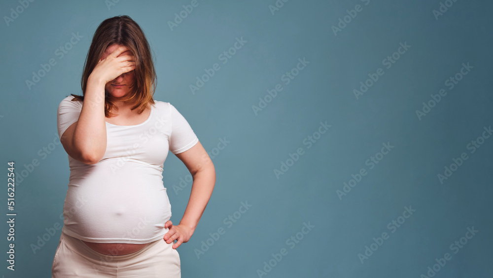 Pensiveness on face of pregnant woman, studio shot on blue background, copy space with a place under the text on the prohibition of abortions Pensiveness on face of pregnant woman, studio shot on blue background, copy space with a place under the text on the prohibition of abortions