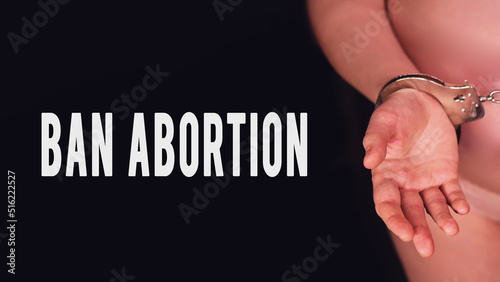 Inscription banning abortion and pregnant woman on a black background handcuffed, close up. Concept of problems with lack of freedom during pregnancy