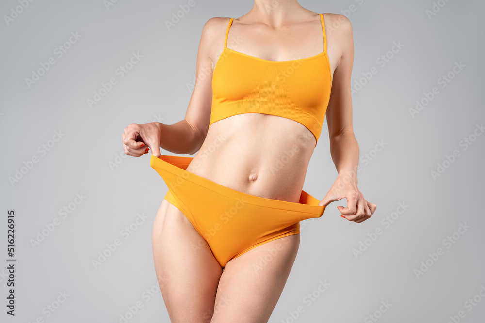 Foto de Slim woman in yellow underwear after weight loss on gray background  do Stock
