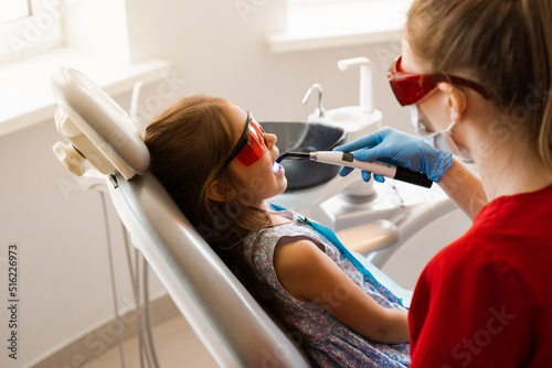 Child dentist treats and removes caries in a patient. Uv illumination of photopolymer tooth filling procedure. Child dentistry.