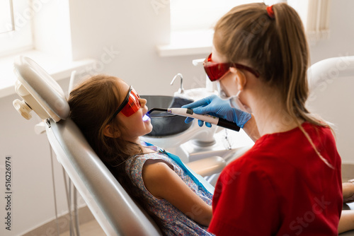 Child dentist treats and removes caries in a patient. Uv illumination of photopolymer tooth filling procedure. Child dentistry.