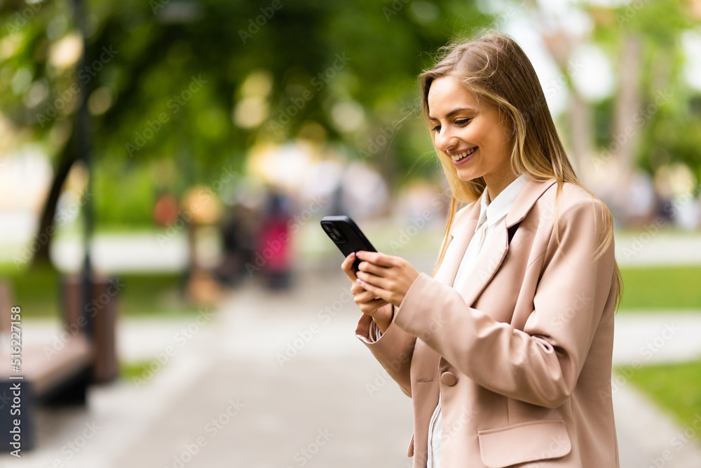Young woman stand in city spring park outdoors use phone chat with boyfriend on social network. People active urban lifestyle concept Young woman stand in city spring park outdoors use phone chat with boyfriend on social network. People active urban lifestyle concept