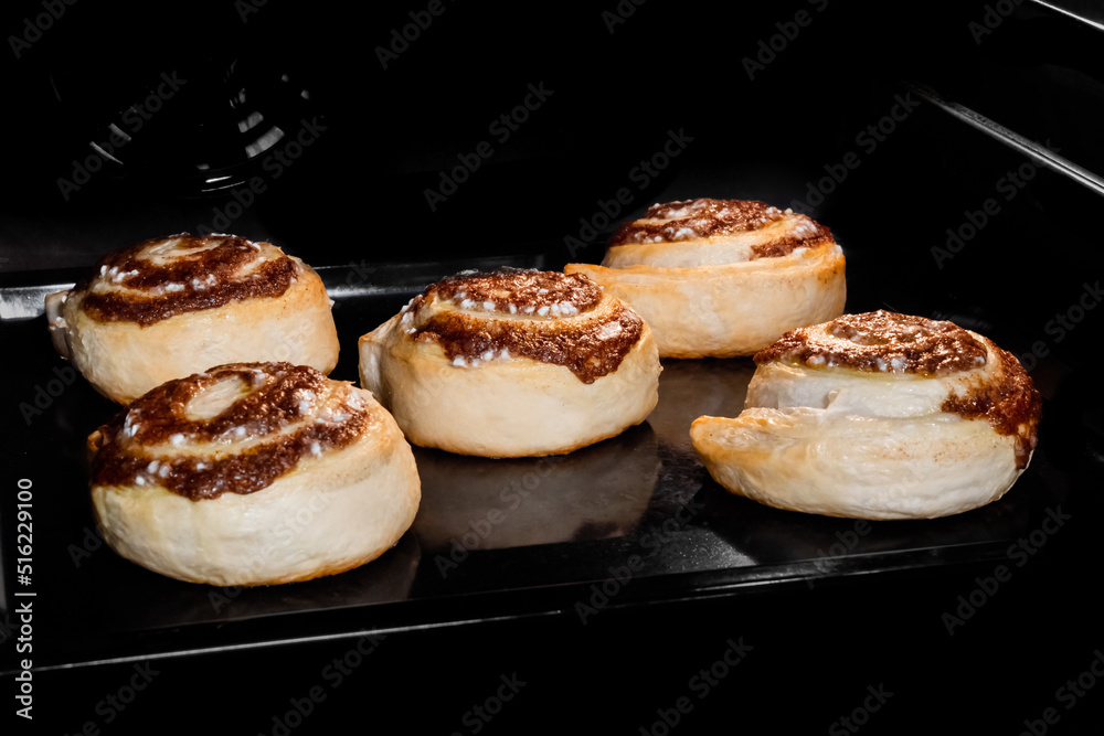 Five cinnamon buns baking and rising on tray in electric oven. Swedish cuisine, homemade bakery, food, cooking and pastry concept