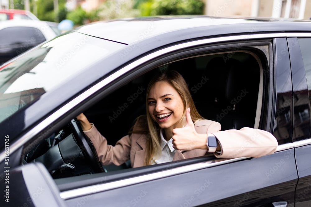Young woman inside a car driving in the street and gesturing thumb up