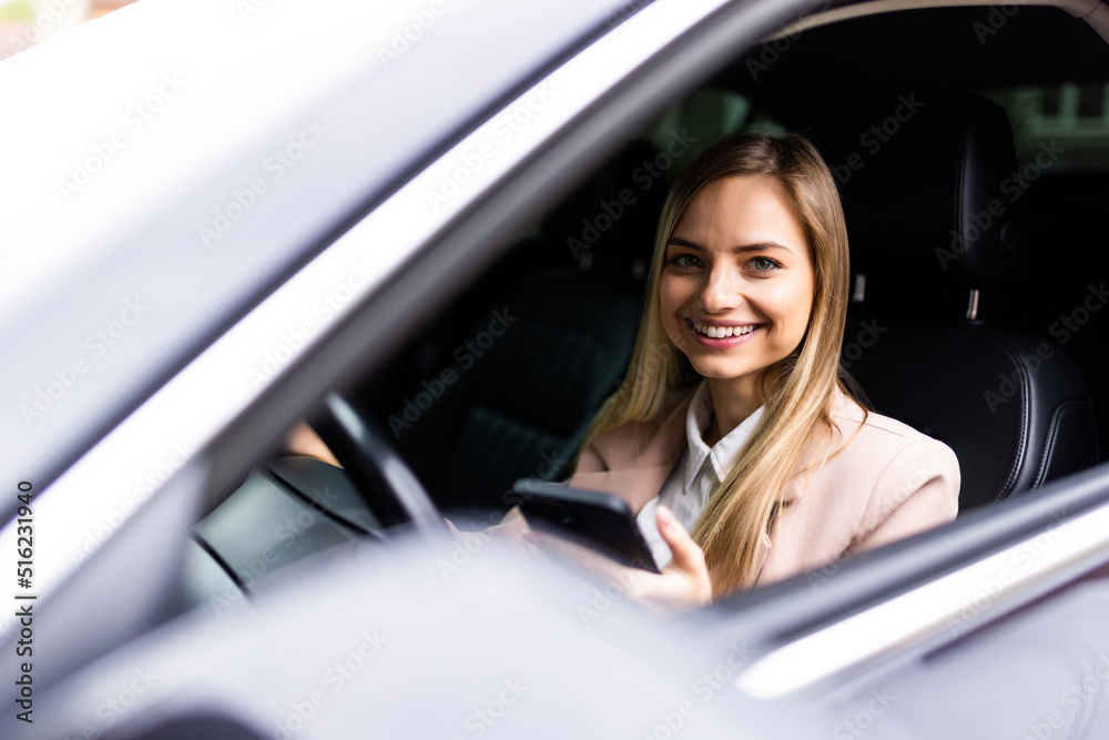 Young business woman sitting in car and using her smartphone.
