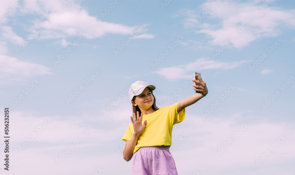 A preteen girl takes a selfie on a mobile phone against a blue sky. Horizontal frame, copy space A preteen girl takes a selfie on a mobile phone against a blue sky. Horizontal frame, copy space