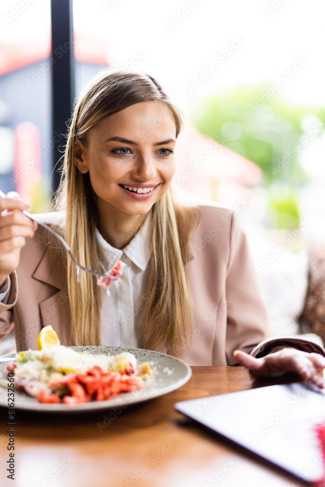 Young woman eating healthy salad on a restaurant terrace, feeling happy on a summer day