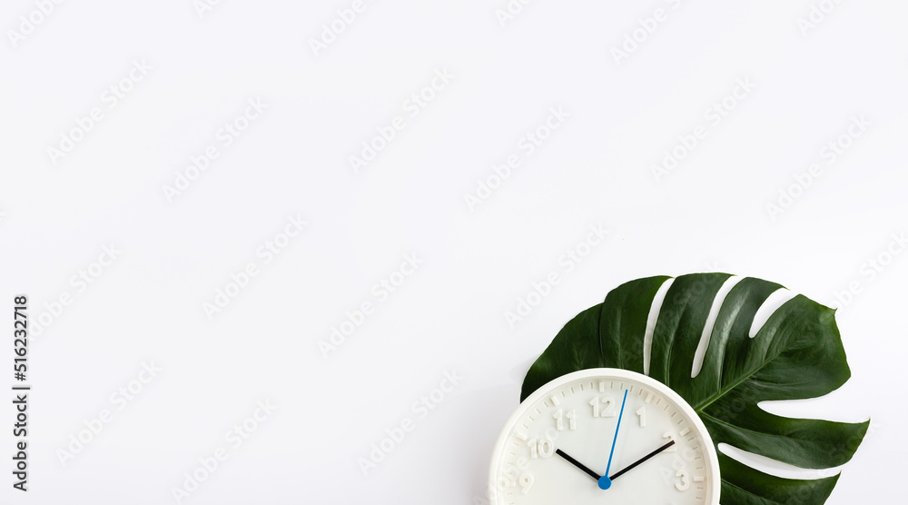 Modern wall clock and green monstera leaf on white background. Slow life concept. Selective focus, copy space Modern wall clock and green monstera leaf on white background. Slow life concept. Selective focus, copy space