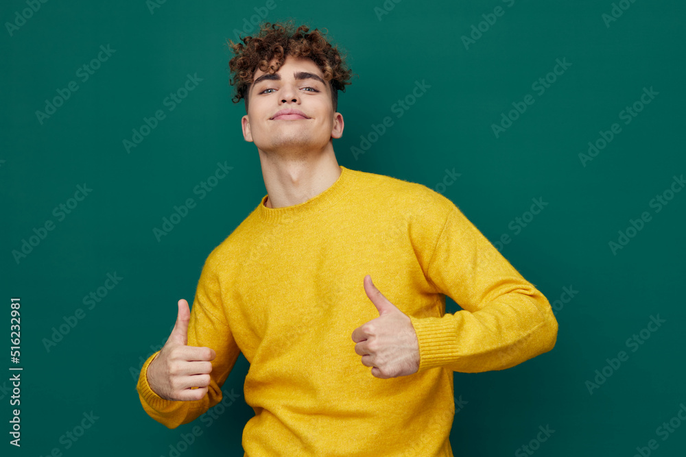 a joyful, smiling man stands on a green background in a yellow sweater and spreads his arms wide apart, making a funny face, showing thumbs up a joyful, smiling man stands on a green background in a yellow sweater and spreads his arms wide apart, making a funny face, showing thumbs up