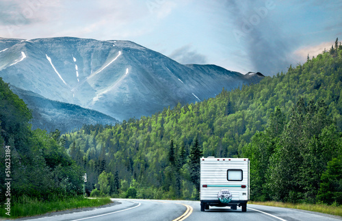 Retro camper driving on highway sucrrounded by evergreen forests and tall mountains with snow patches in distance on overcast day - Kenai Peninsula Alaska