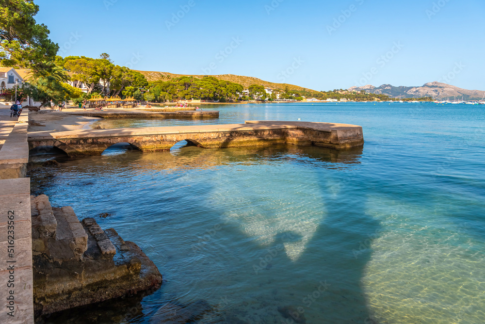 The beach and promenade with the piers of Port de Pollença in the evening at sunset. The beach and promenade with the piers of Port de Pollença in the evening at sunset.