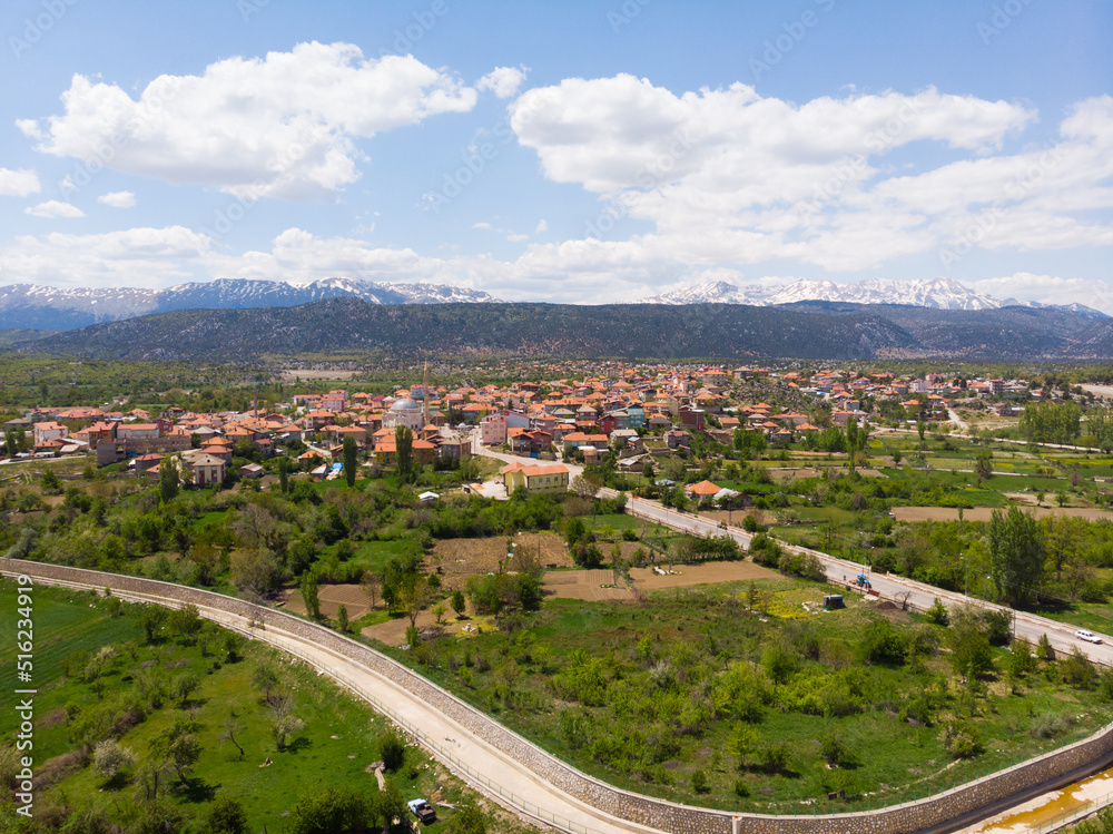 Aerial view of typical Turkish small town Yesildag of Burdur province on sunny spring day with snowy mountain range in background..