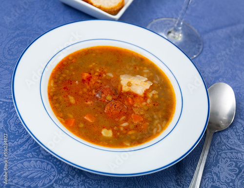 Spicy stewed lentils with suasage and vegetables with thick tomato sauce served in white plate. Typical Spanish cuisine