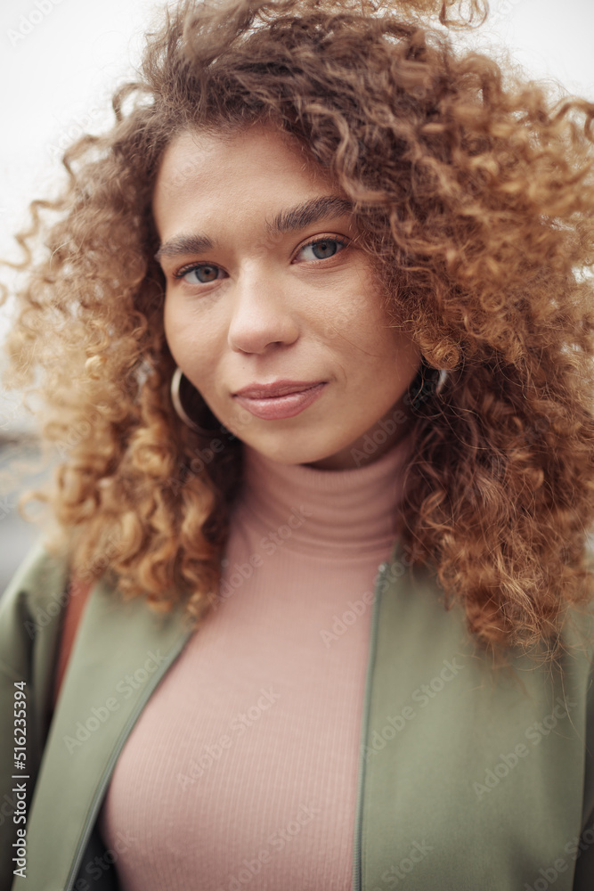 Young pretty woman with long and thick brown wavy hair and natural makeup looking at camera while standing in the street Young pretty woman with long and thick brown wavy hair and natural makeup looking at camera while standing in the street