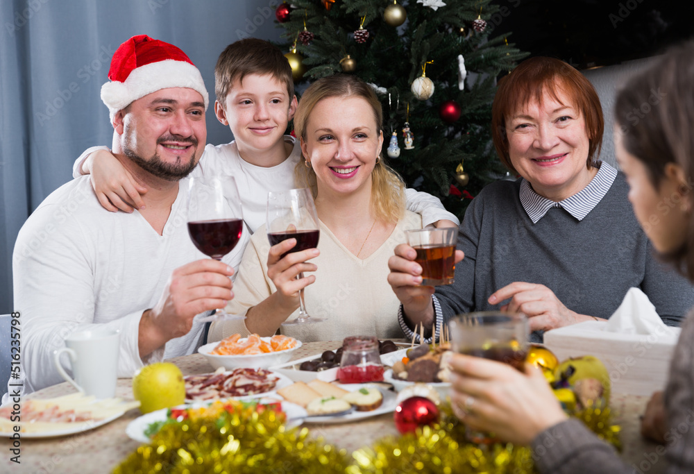 Cheerful family at dining table for Christmas dinner against backdrop of decorated fir tree