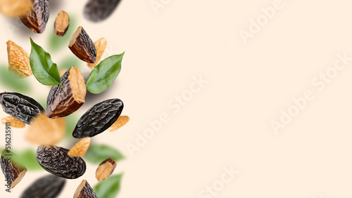 Tonka beans and green leaves levitate on a light beige background. Flying Dipteryx odorata for pastry, confectionery business, cooking, baking and aroma using. Modern fly healthy food, copy space photo