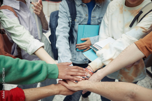 Group of intercultural teenage students in casualwear making pile of hands while standing in circle symbolizing support and unity