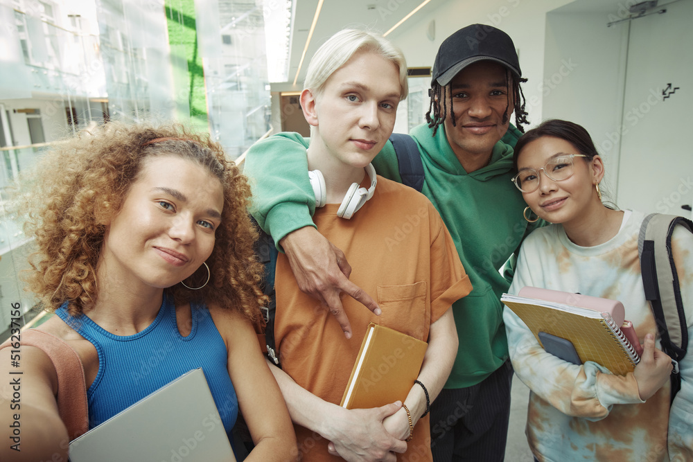 © Seventyfour - Two happy intercultural teenage couples in casualwear looking at camera while making selfie in college corridor at break or after classes