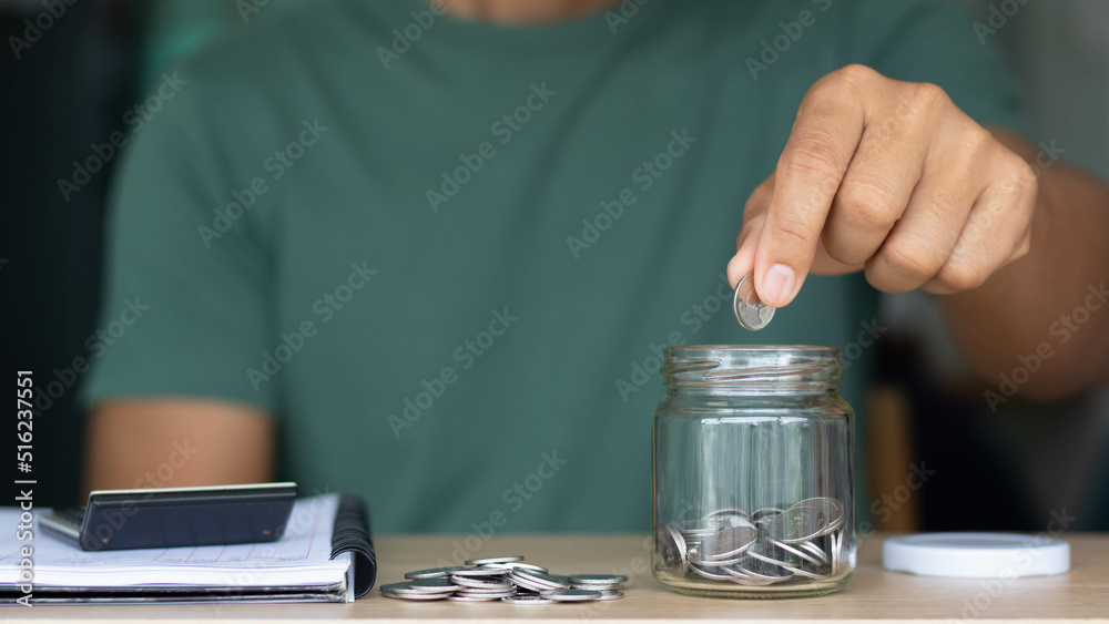 Businessman putting coins in a glass jar with a calculator and notebook. the concept of saving money for the future, Business, finance, accounting, investment, and financial planning. Businessman putting coins in a glass jar with a calculator and notebook. the concept of saving money for the future, Business, finance, accounting, investment, and financial planning.