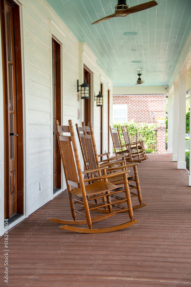 Three vintage brown wooden rocking chairs are on the veranda of an old  white colored country