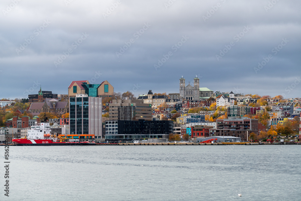 Naklejka premium Daytime downtown St. John's, Newfoundland, under blue skies. Multiple supply vessels docked to support the offshore gas and oil industry. The cityscape has colorful buildings, houses, and churches.
